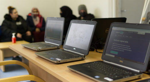Three laptops, with people in the background, blurred.