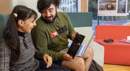 A young man working at a centre shows a tablet to a young woman. They are both smiling and look happy.