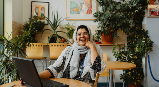 A woman wearing a headscarf using a laptop and smiling at the camera