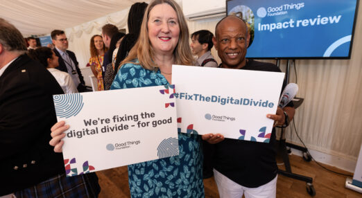 Helen Milner with a member of the National Digital Inclusion Network smiling and holding placards that say we're fixing the digital divide for good.
